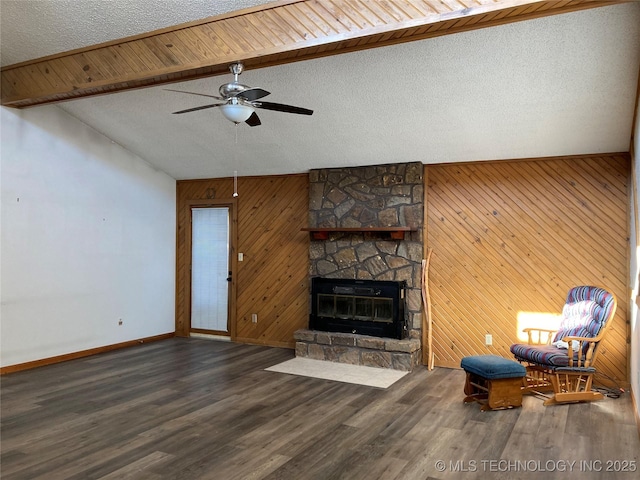 living area featuring dark wood-style flooring, vaulted ceiling with beams, a stone fireplace, a textured ceiling, and baseboards