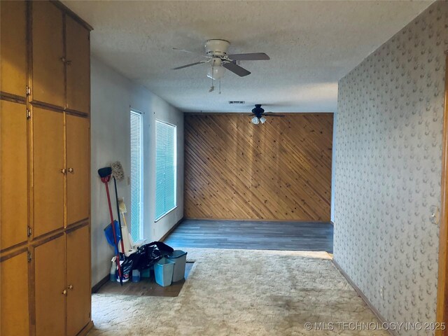 empty room featuring ceiling fan, a textured ceiling, and wood walls