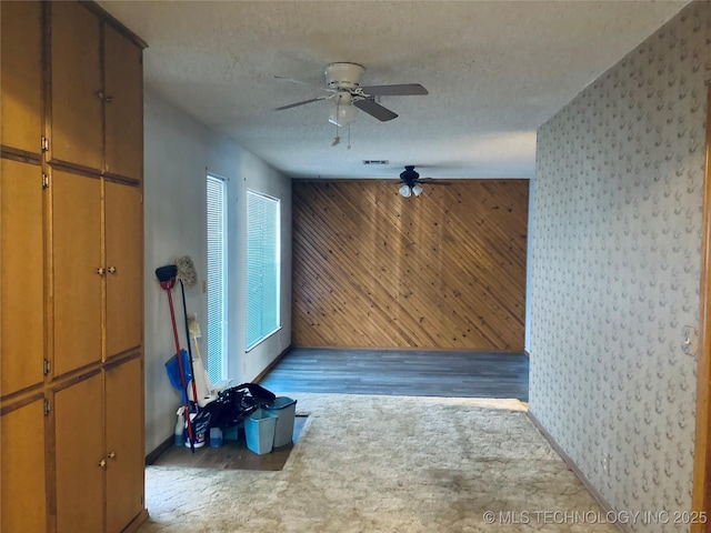 interior space with a textured ceiling, wood walls, light carpet, and visible vents