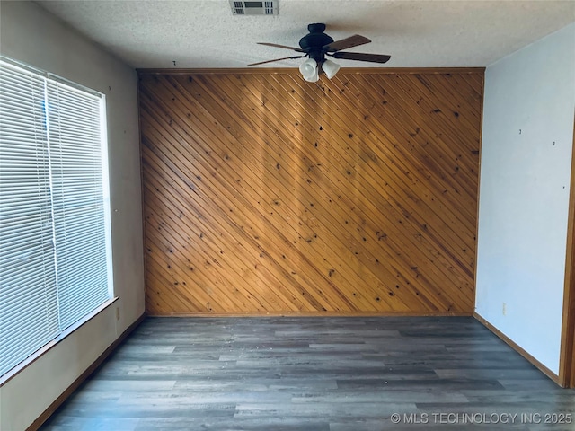 unfurnished room with dark wood-type flooring, visible vents, a textured ceiling, and wooden walls