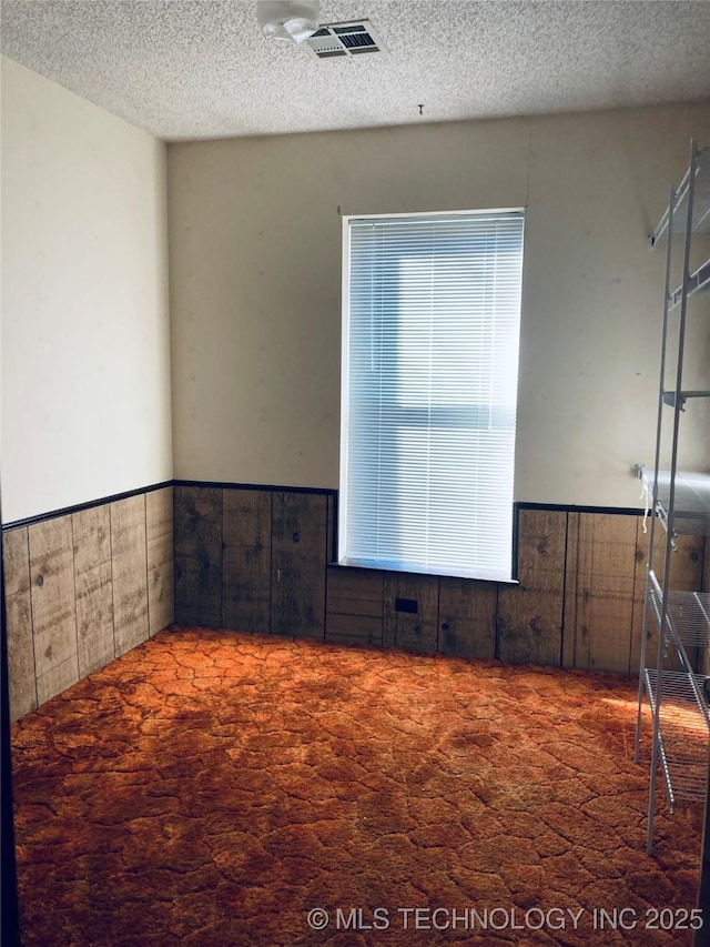 unfurnished room featuring wainscoting, dark carpet, and a textured ceiling