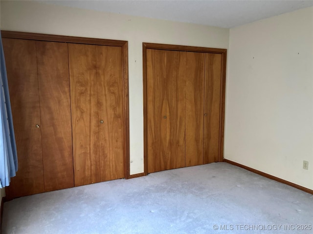 unfurnished bedroom featuring light carpet, baseboards, and two closets