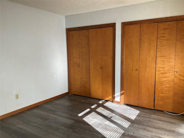 unfurnished bedroom featuring two closets, dark hardwood / wood-style floors, and a textured ceiling