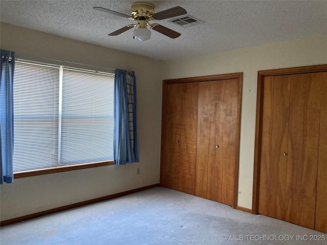 unfurnished bedroom with multiple closets, light colored carpet, visible vents, and a textured ceiling