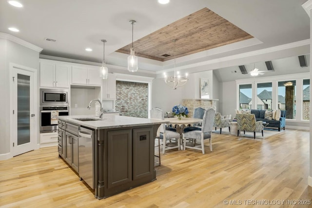 kitchen with stainless steel appliances, a sink, white cabinets, light wood-type flooring, and a tray ceiling