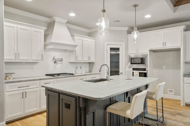 kitchen with a sink, white cabinets, custom range hood, appliances with stainless steel finishes, and crown molding