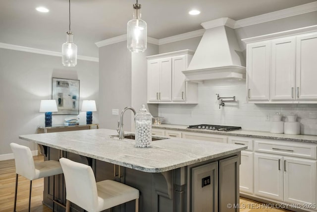 kitchen with stainless steel gas cooktop, custom exhaust hood, decorative backsplash, ornamental molding, and a sink