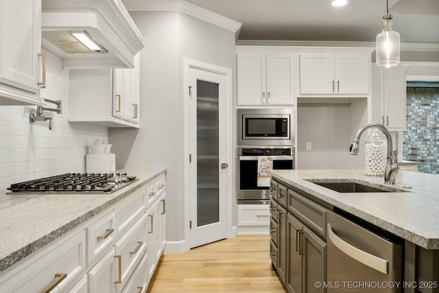 kitchen featuring custom exhaust hood, stainless steel appliances, light wood-style flooring, white cabinets, and a sink