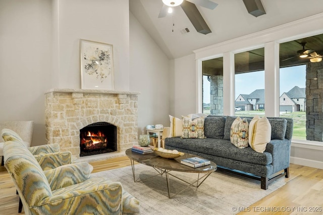 living area featuring visible vents, a ceiling fan, vaulted ceiling, a stone fireplace, and wood finished floors