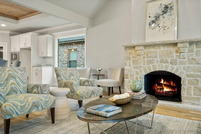 sitting room with a tray ceiling, recessed lighting, light wood-style floors, ornamental molding, and a stone fireplace