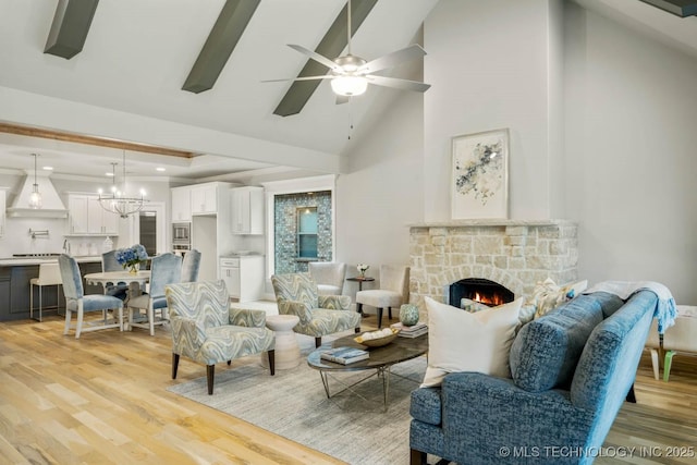 living room with high vaulted ceiling, a stone fireplace, recessed lighting, ceiling fan with notable chandelier, and light wood finished floors