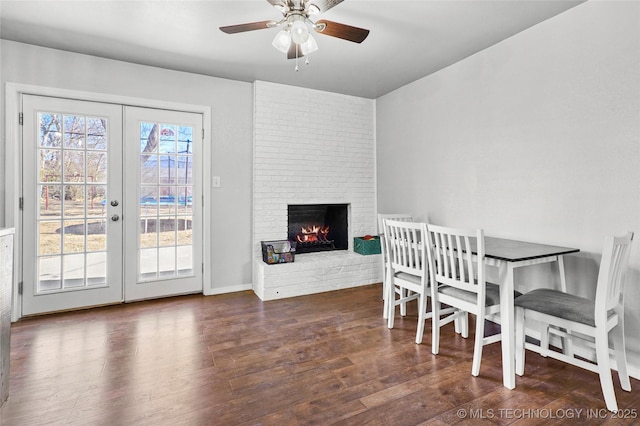 dining area with dark wood-type flooring, a fireplace, french doors, and ceiling fan