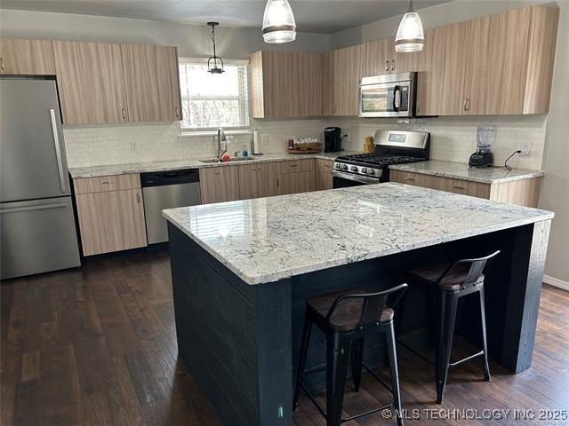 kitchen featuring a kitchen bar, sink, dark hardwood / wood-style floors, pendant lighting, and stainless steel appliances