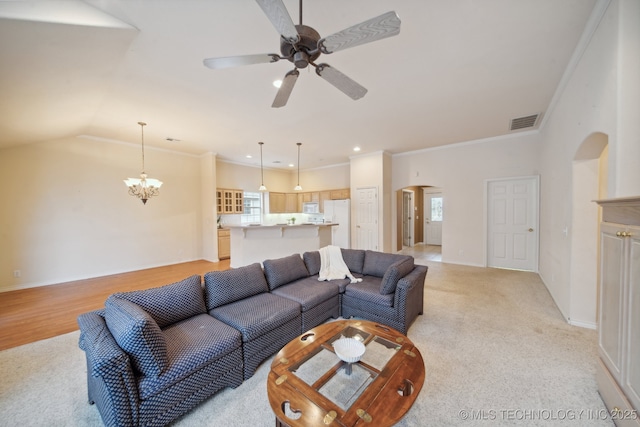 living room with ornamental molding, vaulted ceiling, ceiling fan with notable chandelier, and light colored carpet