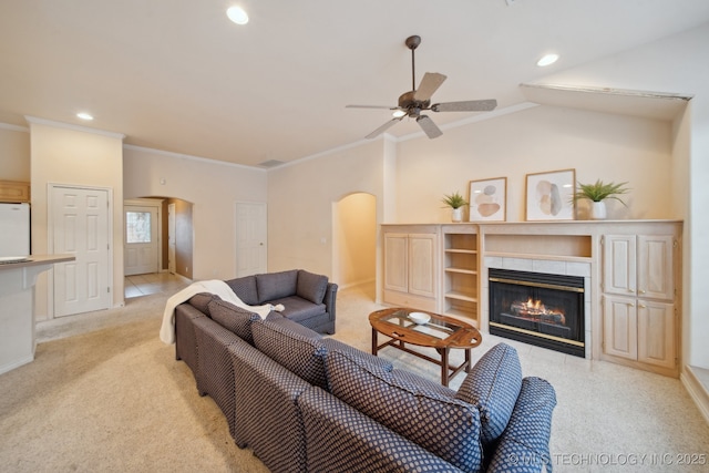 carpeted living room featuring ceiling fan, ornamental molding, a tiled fireplace, and lofted ceiling