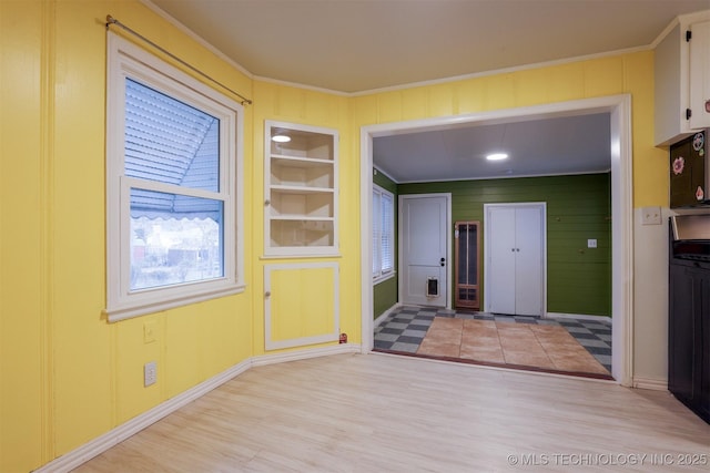 interior space featuring built in shelves, ornamental molding, and light hardwood / wood-style floors