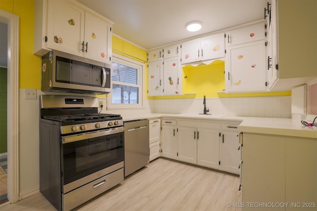 kitchen with appliances with stainless steel finishes, tasteful backsplash, white cabinetry, sink, and light hardwood / wood-style floors