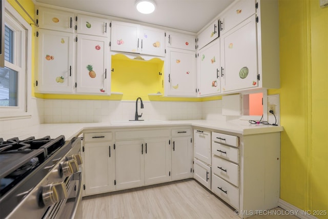 kitchen featuring white cabinetry, sink, stainless steel stove, and backsplash