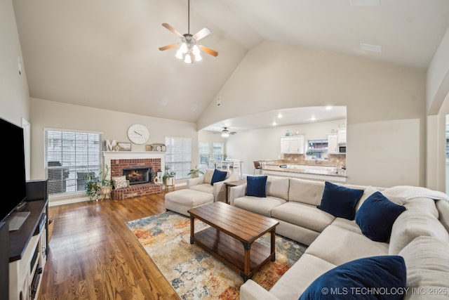 living room featuring dark hardwood / wood-style flooring, a brick fireplace, ceiling fan, and high vaulted ceiling