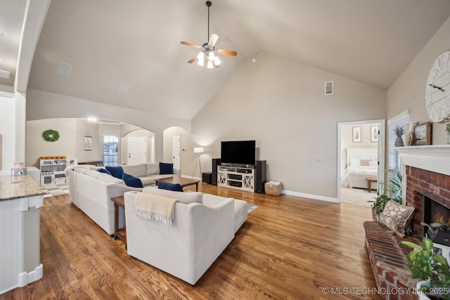 living room with a brick fireplace, light hardwood / wood-style floors, high vaulted ceiling, and ceiling fan