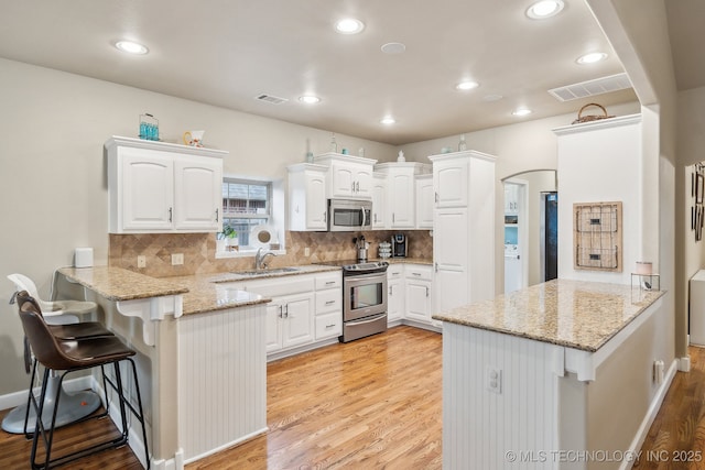 kitchen with stainless steel appliances, kitchen peninsula, white cabinets, and a kitchen bar