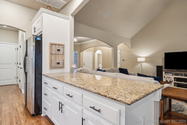 kitchen with lofted ceiling, stainless steel fridge, light stone counters, light hardwood / wood-style floors, and white cabinets