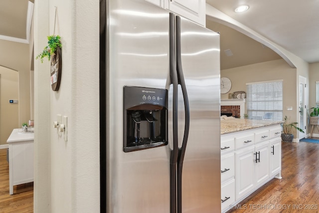 kitchen with light wood-type flooring, light stone countertops, stainless steel fridge with ice dispenser, and white cabinets