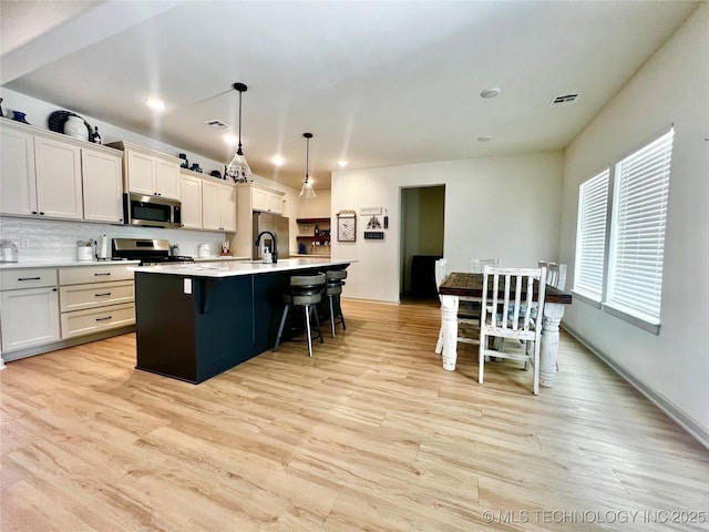 kitchen with a breakfast bar area, decorative light fixtures, a center island with sink, light wood-type flooring, and appliances with stainless steel finishes