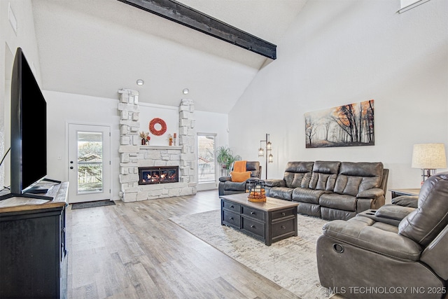 living room featuring beamed ceiling, a fireplace, a wealth of natural light, and light wood-type flooring