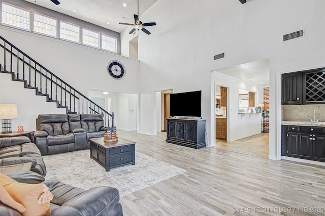 living room with ceiling fan, a towering ceiling, light hardwood / wood-style flooring, and indoor wet bar