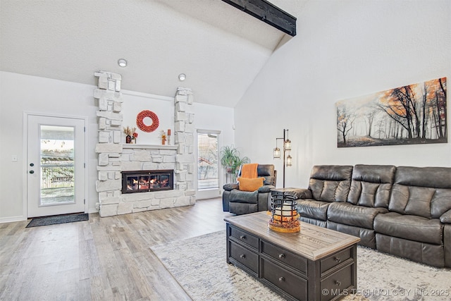 living room featuring a stone fireplace, high vaulted ceiling, a textured ceiling, light wood-type flooring, and beam ceiling