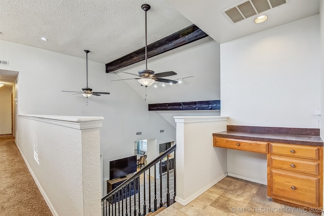 interior space featuring ceiling fan, built in desk, lofted ceiling with beams, and a textured ceiling