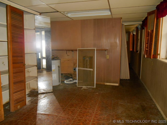 interior space with a drop ceiling, water heater, and wood walls