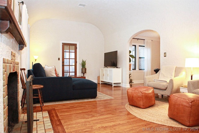 living room with wood-type flooring, vaulted ceiling, and a brick fireplace