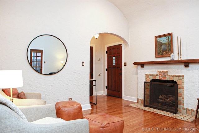 living room with wood-type flooring, a tiled fireplace, and vaulted ceiling