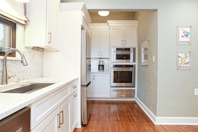 kitchen with dark wood-type flooring, sink, light stone counters, white cabinetry, and stainless steel appliances