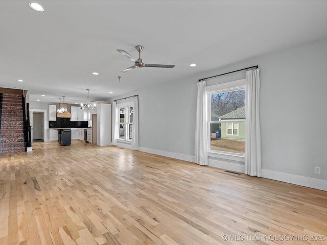 unfurnished living room with ceiling fan with notable chandelier and light hardwood / wood-style floors