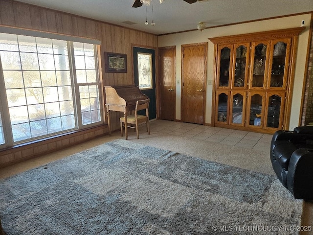 sitting room with ceiling fan, ornamental molding, wooden walls, and carpet floors