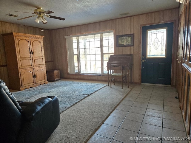 entryway featuring ceiling fan, light colored carpet, wooden walls, and a textured ceiling