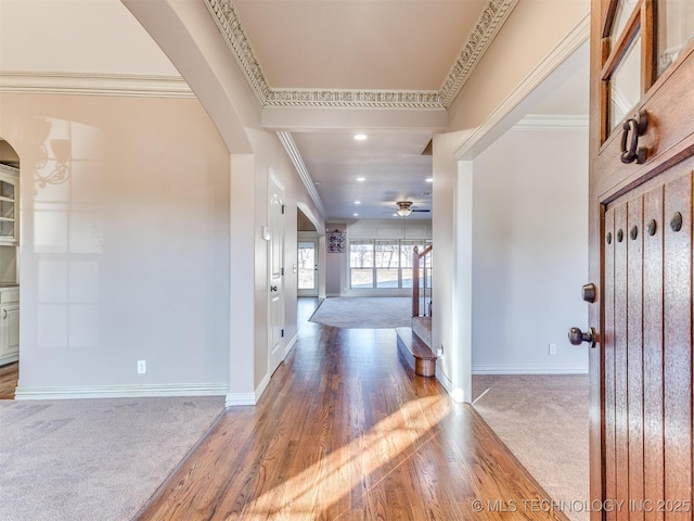 carpeted foyer featuring wood finished floors, arched walkways, crown molding, baseboards, and ceiling fan