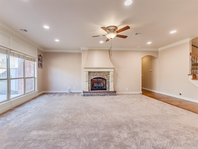 unfurnished living room with visible vents, a stone fireplace, ornamental molding, and a ceiling fan