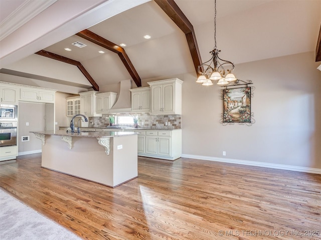 kitchen with appliances with stainless steel finishes, backsplash, lofted ceiling with beams, an island with sink, and white cabinets