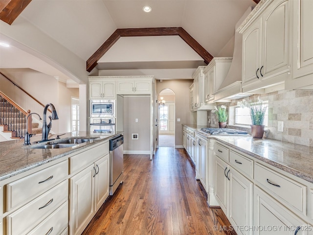 kitchen featuring light stone countertops, arched walkways, stainless steel appliances, a sink, and vaulted ceiling