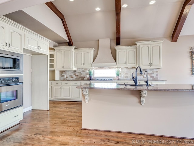 kitchen with tasteful backsplash, premium range hood, white cabinets, and appliances with stainless steel finishes