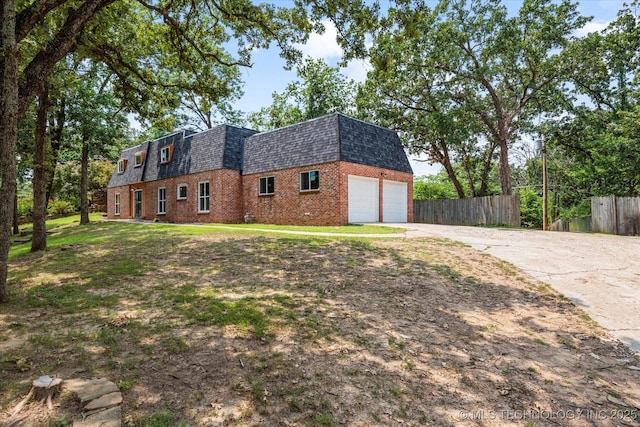 view of home's exterior with mansard roof, concrete driveway, roof with shingles, fence, and brick siding