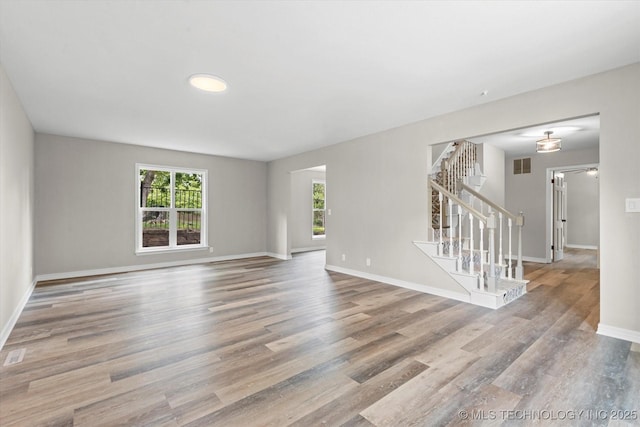 unfurnished room featuring stairway, plenty of natural light, wood finished floors, and baseboards