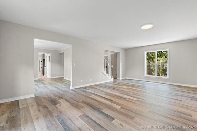 empty room with light wood-style floors, stairs, and baseboards