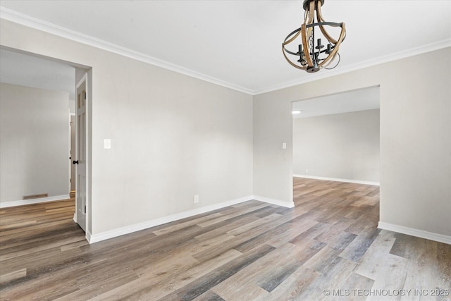 spare room featuring baseboards, a chandelier, wood finished floors, and ornamental molding