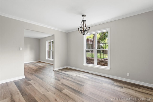 spare room featuring an inviting chandelier, crown molding, baseboards, and wood finished floors