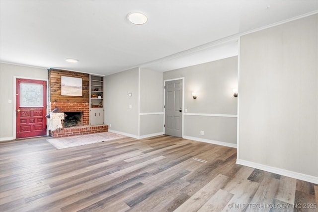 unfurnished living room featuring a brick fireplace, built in features, light wood-style flooring, and baseboards